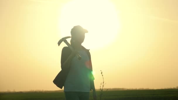 Una contadina porta una pala sulle spalle e va in un campo di terra in un ranch a gocciolare un orto, un giardiniere lavora in un giardino, scavando e piantando piante a terra. — Video Stock