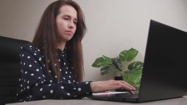 Una mujer de negocios trabaja en una computadora en la oficina, un freelancer escribe texto en el teclado, en línea en un programa de forma remota, Internet para la transferencia de datos, una chica llena y mantiene importante — Vídeos de Stock