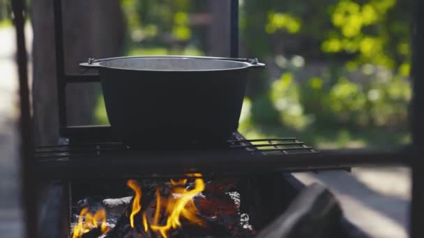 Panci masak berdiri di atas kisi-kisi dengan api besar, memasak di luar ruangan dalam panci, resep wisata luar ruangan, hidangan api pada akhir pekan, bersantai di hutan — Stok Video