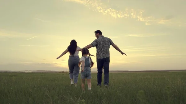 Una familia feliz corre a través del campo con un niño pequeño al atardecer en el cielo, mamá corriendo, papá y el niño están saltando alegremente en el campo por la noche, el equipo está viajando alegremente jugando —  Fotos de Stock