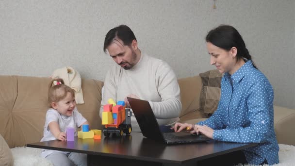 Мама працює позаштатним працівником комп'ютера вдома, діти і тато грають з кольоровими кубиками, розвивають навички дитячого мотору, сімейний спосіб життя, батьки виховують маленьку дочку. — стокове відео
