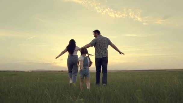 Een gelukkig gezin rent over het veld met een klein kind bij zonsondergang in de lucht, rennende mama, papa en kind springen vrolijk in het veld in de avond, het team reist vrolijk spelend — Stockvideo