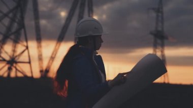 Yüksek elektrik santrallerinin arka planında bir elektrikçi elektrik yapısının geliştirilmesi projesine bakıyor, kablolardaki elektrik voltajının genişletilmesi