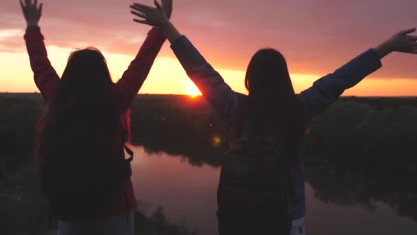 Gelukkig actieve hipster meisjes met rugzakken op hun rug springen bij zonsondergang in de lucht met hun handen omhoog, duizendjarige vrouw reiziger op een hoge berg, bereiken het doel en verheugen zich in de overwinning — Stockvideo
