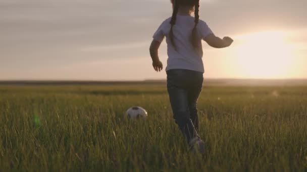 Klein kind rent over het groene voetbalveld voetballen bij zonsondergang in de lucht, kind schopt de bal en haalt hem in, het concept van een gelukkig kinderleven, actieve gezonde baby — Stockvideo