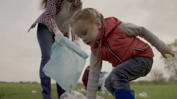 Un niño pequeño recoge basura con sus padres, el concepto de una familia feliz, salvar un planeta verde limpio, limpiar el área de residuos innecesarios sucios, acumulaciones de basura después de que la gente descanse en — Vídeos de Stock