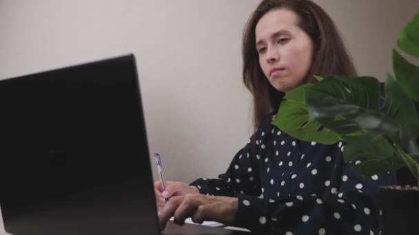 Una mujer de negocios trabaja en una computadora en la oficina, un freelancer escribe texto en el teclado, en línea en un programa de forma remota, Internet para la transferencia de datos, una chica llena y mantiene importante — Vídeos de Stock