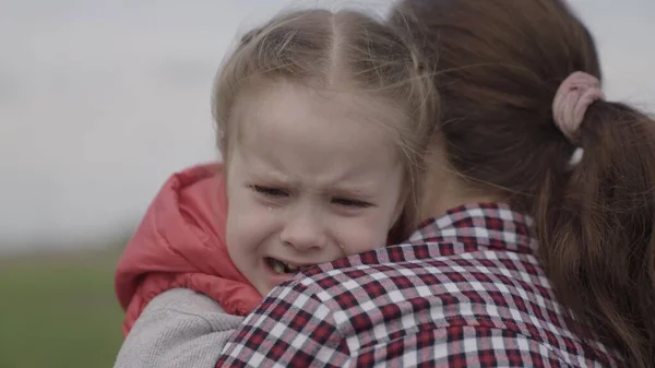 Maminka uklidňuje dítě. dítě pláče v parku v náručí mámy. rodinná matka a dítě se slzami v očích objímají svou matku, emocionálně. milující mladá matka objímá a uklidňuje svou malou dcerku — Stock fotografie