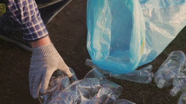 Male hand collects garbage in a garbage bag close-up, rid the planet of a garbage dump of plastic, bottles, glasses, napkins, volunteer work to clean the earths surface — Stock Photo, Image