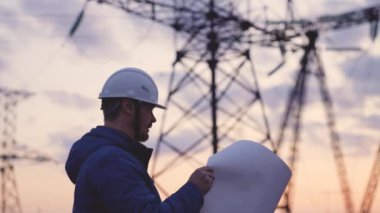 Yüksek elektrik santrallerinin arka planında bir elektrikçi elektrik yapısının geliştirilmesi projesine bakıyor, kablolardaki elektrik voltajının genişletilmesi