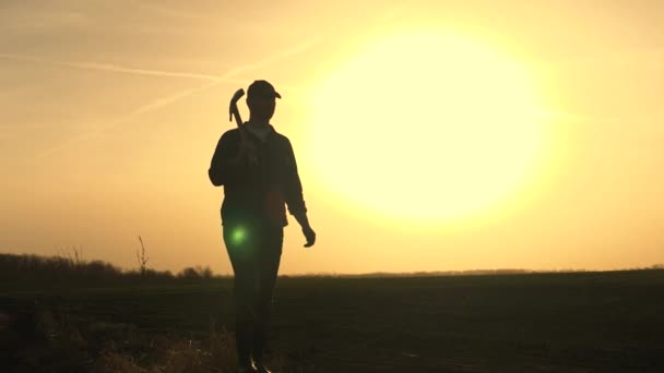 Un agricultor camina por el campo con una pala en botas de goma para cavar el suelo de la tierra al atardecer, la agricultura, la tierra, el cultivo de verduras, bayas y frutas, la plantación de plántulas, la temporada de excavación — Vídeo de stock