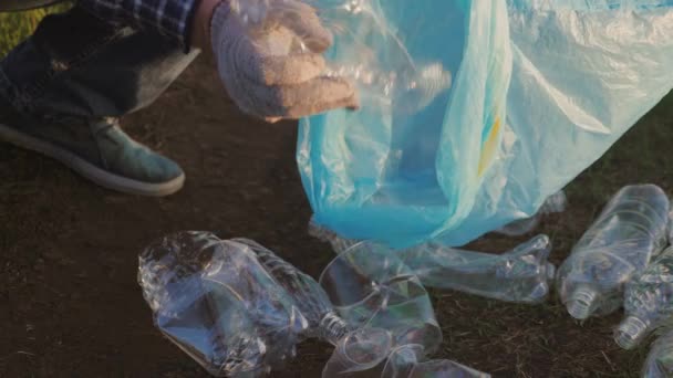 Mão masculina coleta lixo em um saco de lixo close-up, livrar o planeta de um depósito de lixo de plástico, garrafas, copos, guardanapos, trabalho voluntário para limpar a superfície da terra — Vídeo de Stock