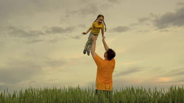 Małe szczęśliwe dziecko lata jak samolot na tle nieba w zielonej pszenicy, koncepcja szczęśliwej rodziny z tatą, wesołe życie dzieci, dziecko śmieje się w rękach ojca — Zdjęcie stockowe