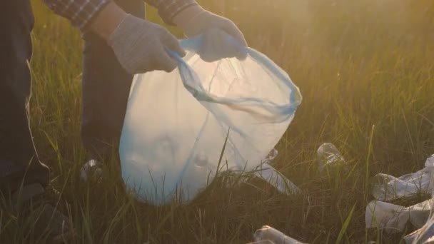 Un uomo in guanti protettivi raccoglie immondizia con le mani in un sacco della spazzatura, volontariato nella natura all'aperto, pulizia bottiglie di plastica, bicchieri, tovaglioli su erba verde, eco, inquinamento della natura — Video Stock