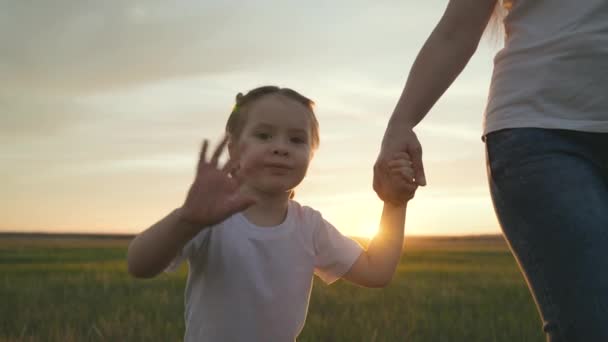 Mom leads a little girl by the hand, waving her hand in the glare of the sunset, a dream to be a happy family, a close-up of a smiling child, hold a childs hand in an older hand, motherly love and — Stock Video