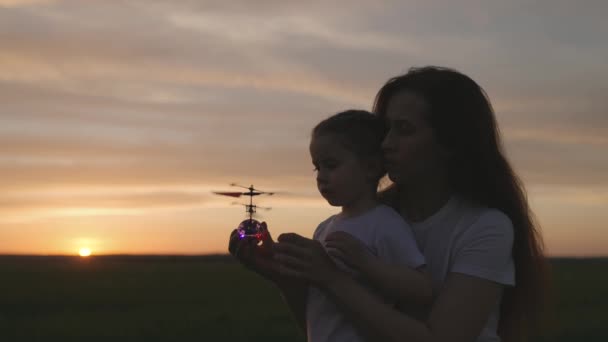 Gyermek anya indít egy játék helikopter naplementekor az égbe, oktatási játékok fejlesztésére gyermek gondolkodás, boldog családi koncepció, anyai gondoskodás ölelés gyerek, csapatmunka — Stock videók