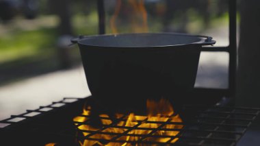 Tencere ızgaranın üzerinde büyük bir ateş alevi, açık havada bir tencerede yemek pişirme, açık hava turist tarifleri, hafta sonları ateşli yemekler, ormanda dinlenme.