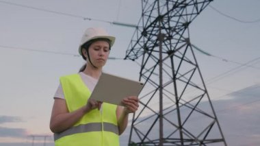 Bir elektrikçi, elektrik sağlayan büyük bir enerji santralinde tabletle çalışır, bir enerji mühendisi yüksek voltaj kulelerinden bir proje yapar, modern teknolojileri kullanarak kablolardan akım geçirir.