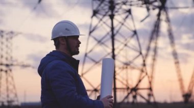 Yüksek elektrik santrallerinin arka planında bir elektrikçi elektrik yapısının geliştirilmesi projesine bakıyor, kablolardaki elektrik voltajının genişletilmesi