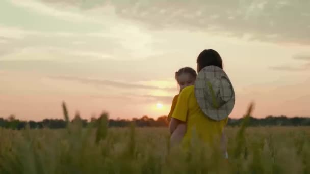 Een vriendelijke boer moeder met een kind in een veld met tarwe bij zonsondergang, graan verbouwen voor het maken van brood, een gelukkig kind, een familiebedrijf op een ranch, het onderzoeken van de gewassen met een baby in haar armen — Stockvideo
