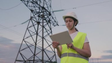 Bir elektrikçi, elektrik sağlayan büyük bir enerji santralinde tabletle çalışır, bir enerji mühendisi yüksek voltaj kulelerinden bir proje yapar, modern teknolojileri kullanarak kablolardan akım geçirir.