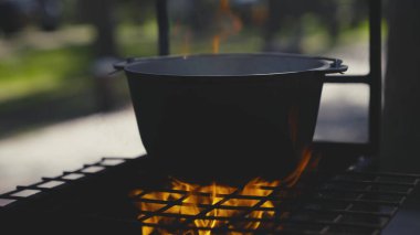 Tencere ızgaranın üzerinde büyük bir ateş alevi, açık havada bir tencerede yemek pişirme, açık hava turist tarifleri, hafta sonları ateşli yemekler, ormanda dinlenme.