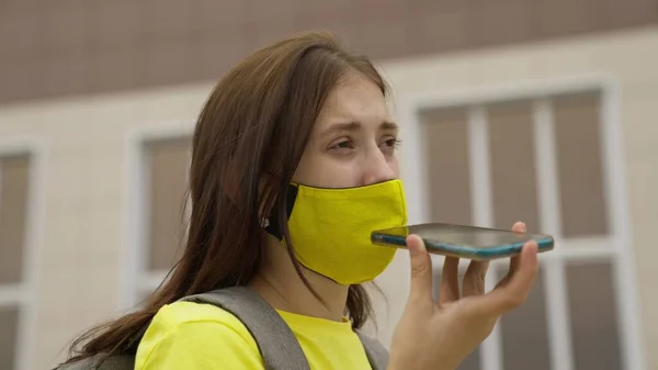 Colegiala en una máscara con una mochila habla en un teléfono inteligente en línea, las tendencias modernas en el progreso tecnológico, protegerse de la infección por coronavirus, filtración de aire —  Fotos de Stock