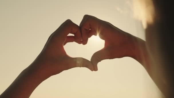 A girl shows her heart with her hands at sunset, a tourist trip, a romantic health vacation, dreaming to love life, an active lifestyle, a dream of a happy relationship with a loved one — Stock Video