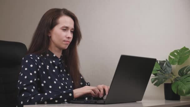 Mulher de negócios séria está sentada no computador e digitando um documento no teclado, olhando para a câmera, a garota freelancer está ocupada, o conceito de um projeto de negócios feliz on-line — Vídeo de Stock