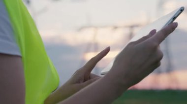 Bir elektrikçi yüksek elektrik santralinde bir tablette çalışır, elleri yakındır, bir enerji işçisi, yüksek voltaj altında, bir cihaz üzerinde yapılan çalışmaların raporunu basar,