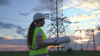 Yüksek elektrik santrallerinin arka planında bir elektrikçi elektrik yapısının geliştirilmesi projesine bakıyor, kablolardaki elektrik voltajının genişletilmesi