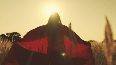 Mutlu kız süper kahramancılık oynuyor kırmızı pelerinli yeşil alanda koşuyorlar, pelerin rüzgarda titriyor. Çocuk oyunları ve hayalleri. Ağır çekim. Genç kızlar süper kahraman olma hayalleri kurar. Kırmızı pelerinli genç kızlar