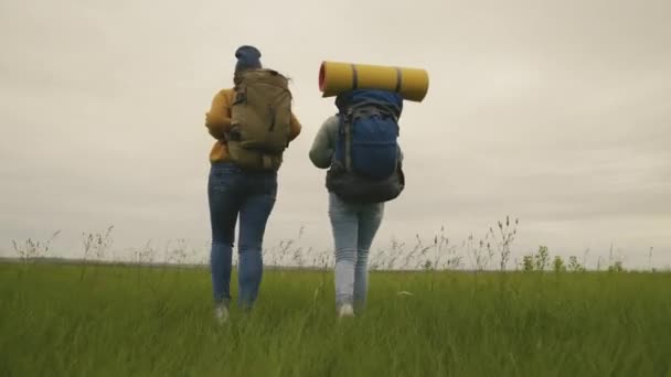 Szczęśliwe tysiącletnie hipsterki podróżują wzdłuż doliny z plecakami, dziewczyny spędzają razem weekendy na kempingu, aktywnym stylu życia, zwiedzając okolicę w poszukiwaniu przygody — Wideo stockowe