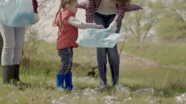 Küçük çocuk parkta ailesi olan çöpleri topluyor, gençlerden gönüllü takım çalışması yapıyor, birlikte gezegeni temizleyeceğiz, plastik tabaklar, şişeler, peçeteler, dünyadaki insanların ekolojik yaşamı...