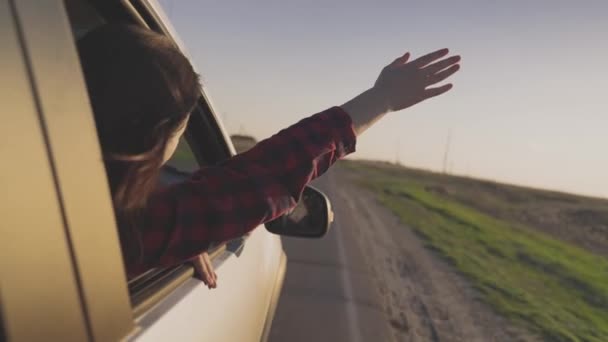 Una joven hermosa chica está comiendo en el coche, asomándose por la ventana del coche, atrapando el viento rukuy, viajando en transporte, divertidas aventuras en la carretera, un viaje de negocios en el camino, ir de vacaciones — Vídeos de Stock