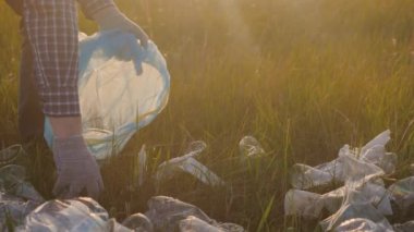 Çevre, yeşil gezegeni temizlemek için gönüllü iş, eko, gün batımının parıltısı altında yeşil çimlerde çöp toplamak, plastik atık şişeleri, gözlük, koruyucu eldivenlerle zarar görmeyen elleri korumak