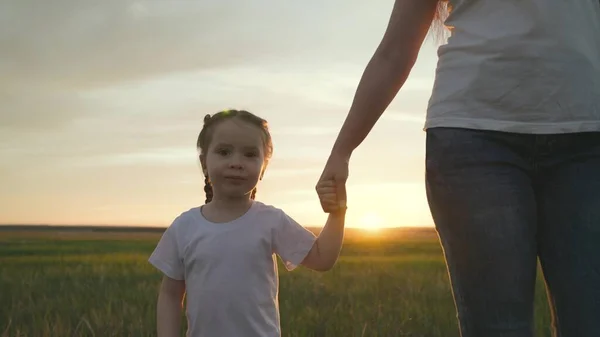 Mom leads a little girl by the hand, waving her hand in the glare of the sunset, a dream to be a happy family, a close-up of a smiling child, hold a childs hand in an older hand, motherly love and — Stock Photo, Image