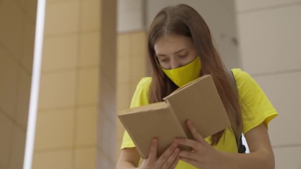 У масках школярка читає книгу на шкільному подвір'ї, учень викладає уроки, літературне читання, освітню програму для підлітків, дівчина з рюкзаком повторює тему з'їденого уроку — стокове відео