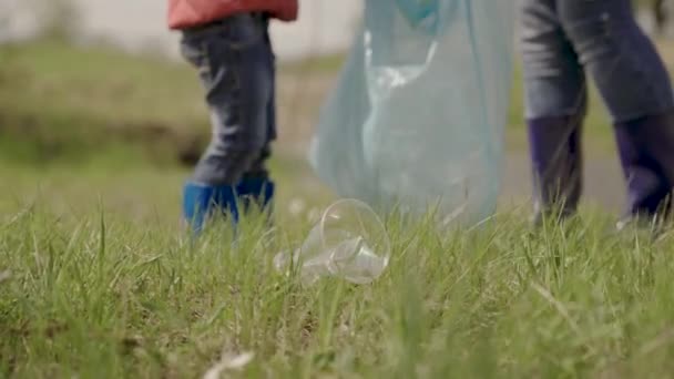 Un niño pequeño en un equipo de voluntarios, un niño limpia la basura de plástico en el suelo, una niña con una familia que limpia la naturaleza de la contaminación, el bebé ayuda al mundo a ser más limpio, el medio ambiente, el trabajo en equipo, la familia feliz — Vídeos de Stock