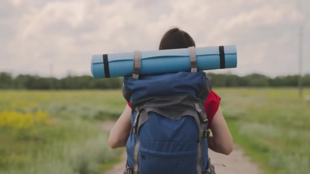 Ενεργό κορίτσι με σακίδιο αναπαύεται σε ένα ταξίδι κάμπινγκ, ένας ταξιδιώτης χιλιετηρίδας, πεζοπορία στη φύση, τον τρόπο ζωής ενός σύγχρονου ανθρώπου, περπατώντας σε ένα χωματόδρομο, αργή κίνηση — Αρχείο Βίντεο