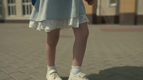 Een klein meisje loopt langs de schoolweg met een rugzak, sneakers op haar voeten close-up, een actief kind na een schooldag, het krijgen van basisonderwijs in een kleuterschool, een kinderdroom om te studeren — Stockvideo