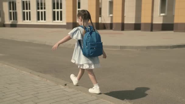 Una niña con una mochila va a la escuela en el patio de la escuela, programa educativo para los niños de la escuela primaria, caminar en la acera y jugar divertido, la vida de los niños en nuevos conocimientos, sueño de la infancia — Vídeos de Stock