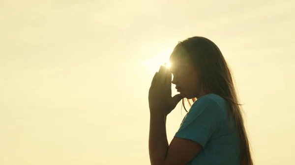 A girl prays at sunset, be a religious person, believe in kindness, a childhood dream, pray looking at the sky in the glare, the inspiring mystery of a childs spiritual emotion, meditation at dawn — Stock Photo, Image