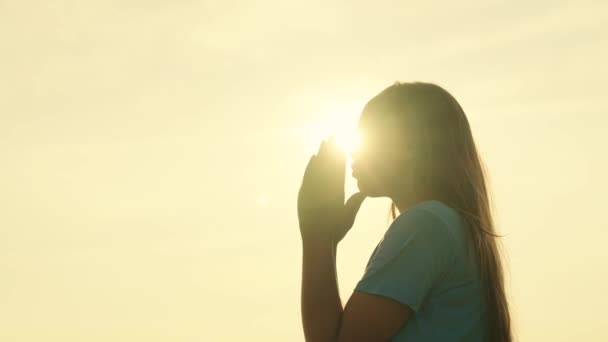 Egy lány imádkozik naplementekor, vallásos ember lesz, hisz a kedvességben, a gyerekkori álomban, imádkozik, hogy az égre nézzen a fényben, a gyermekek spirituális érzelmeinek inspiráló misztériuma, a hajnali meditáció. — Stock videók