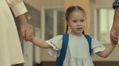 Küçük kız, anne babasıyla el ele okula gidiyor, sırtında sırt çantası olan bir çocuk, ilkokulda öğretmenlik yapıyor, okul eğitimi hakkında bilgi veriyor, mutlu bir aile.