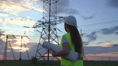 Yüksek elektrik santrallerinin arka planında bir elektrikçi elektrik yapısının geliştirilmesi projesine bakıyor, kablolardaki elektrik voltajının genişletilmesi