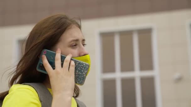 Schoolmeisje meisje in een masker met een rugzak gesprekken op een smartphone online, moderne trends in de technologische vooruitgang, zichzelf te beschermen tegen coronavirus infectie, luchtfiltratie — Stockvideo