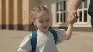 Baba çocuğu elden okula götürüyor, yakın plan, sırt çantalı küçük bir okul kızı, mutlu bir aile, çocukluk hayali, aktif bir öğrenci kız, iyi bir modern eğitim, sevgi ve bilgi.