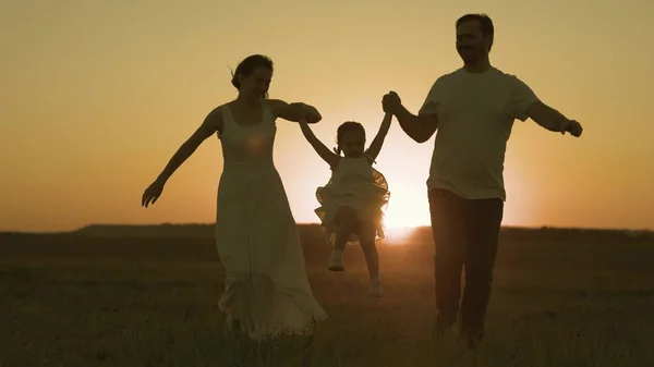 Happy father and mother run across field with small child sunset in sky, silhouette cheerful family, childhood dream of parents, play together, give attention to children, love of mom and dad for kid — Stock Photo, Image
