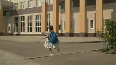 İlkokul çocuğu okul bahçesinde omuzlarında sırt çantasıyla koşuşturuyor, küçük çocuk birinci sınıf öğrencisi, modern müfredat, sokakta aktif bir çocuk, akıllı, mutlu bir kız olma arzusu.